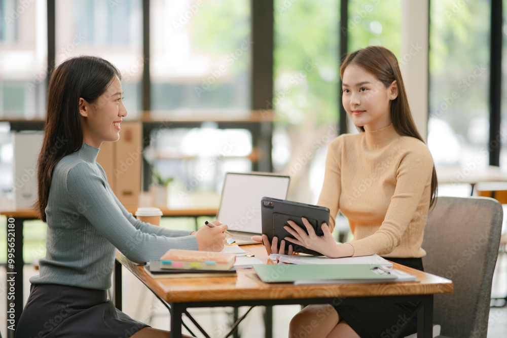 Two women work with tablets, work and chatting about paperwork and graphs. Two women work with tablets, work and chatting about paperwork and graphs.