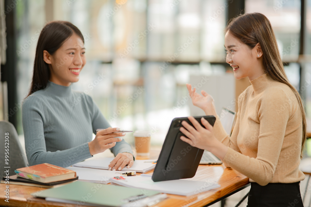 Two women work with tablets, work and chatting about paperwork and graphs. Two women work with tablets, work and chatting about paperwork and graphs.