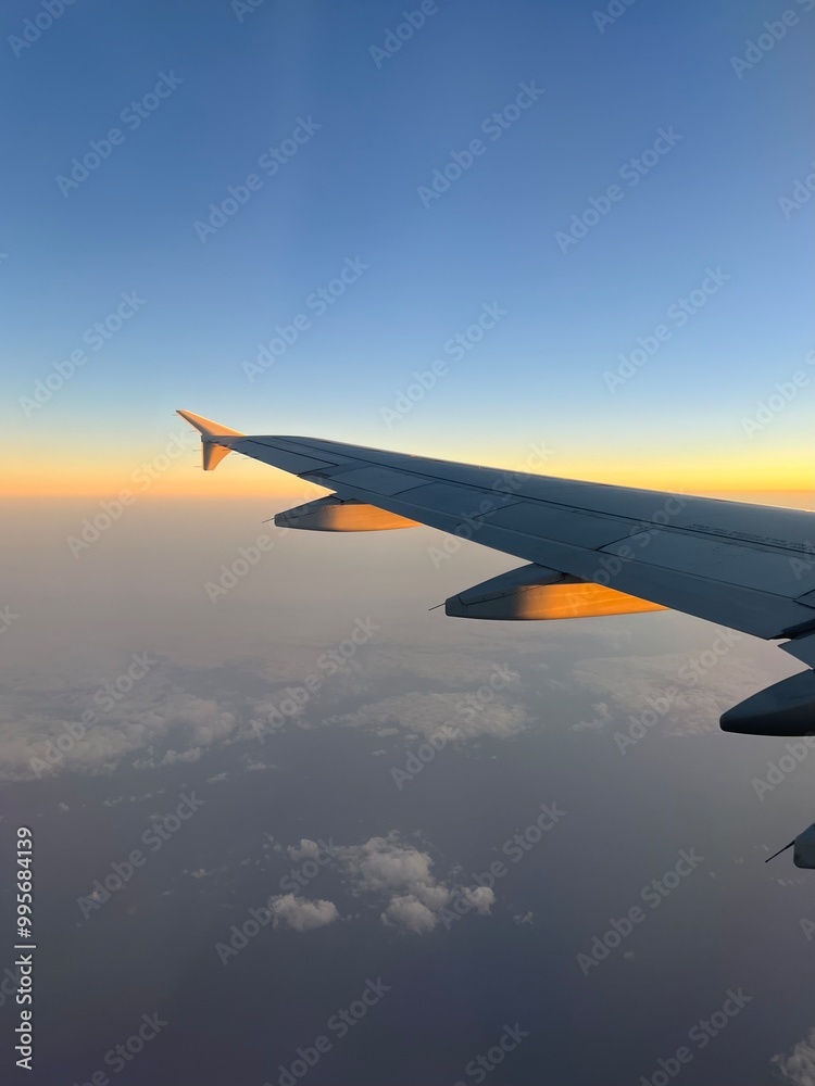Breathtaking view of white wing of aircraft flying in blue sky over colorful fluffy cumulus clouds in sunset Breathtaking view of white wing of aircraft flying in blue sky over colorful fluffy cumulus clouds in sunset