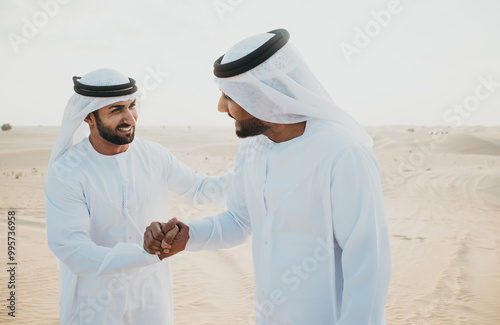 Two business men wearing traditional uae white kandura spending time in the desert of Dubai. Businessmen planning new projects for the construction business in the united arab emirates. photo