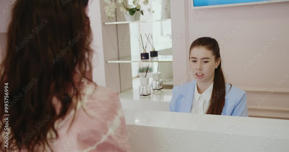 A young woman engaging in a conversation with reception staff in a contemporary spa setting. Young Woman Consulting at Modern Reception Desk in Spa A young woman engaging in a conversation with reception staff in a contemporary spa setting. Young Woman Consulting at Modern Reception Desk in Spa