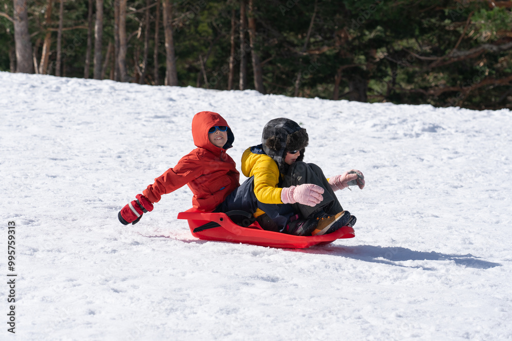 Two children riding together on a sled in the snow enjoying Two children riding together on a sled in the snow enjoying