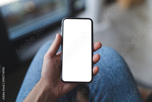 Hand holds phone with white screen, blurred indoor setting and seated figure visible