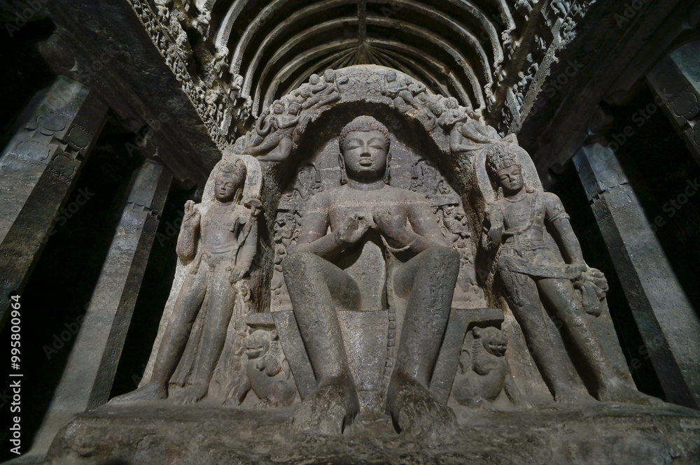 Large stone carved statue of Buddha in meditative posture accompanied by two sculptures one on either side at Ellora cave complex, Maharashtra, India. Large stone carved statue of Buddha in meditative posture accompanied by two sculptures one on either side at Ellora cave complex, Maharashtra, India.