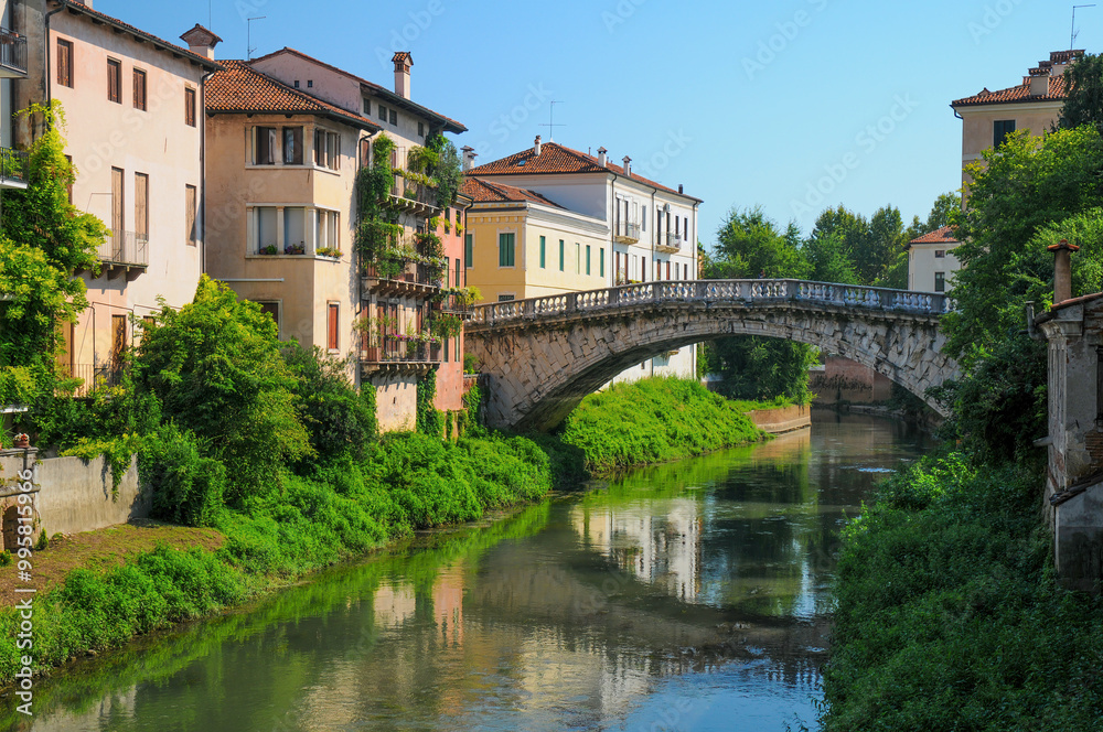 Charming view of a historic stone bridge over a tranquil canal in Vicenza, Italy. Colorful buildings and lush greenery line the waterway, creating a idyllic Italian cityscape Charming view of a historic stone bridge over a tranquil canal in Vicenza, Italy. Colorful buildings and lush greenery line the waterway, creating a idyllic Italian cityscape