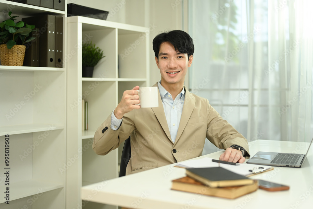 Portrait of confident young businessman holding cup of coffee sitting at his workplace Portrait of confident young businessman holding cup of coffee sitting at his workplace