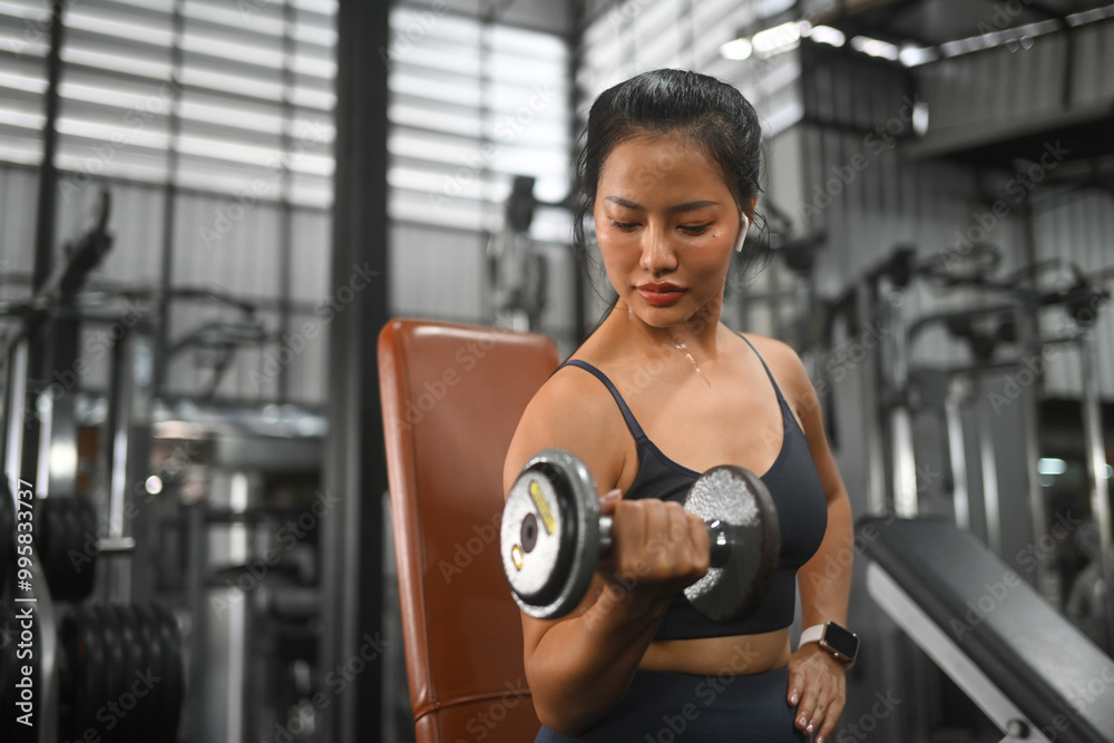 Strong athletic woman doing a bicep curl with weights in a gym Strong athletic woman doing a bicep curl with weights in a gym