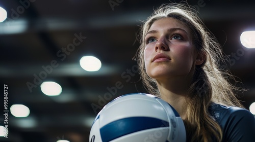 A focused female volleyball player holds a ball, illuminated by spotlights in an indoor arena, creating a determined and intense atmosphere.