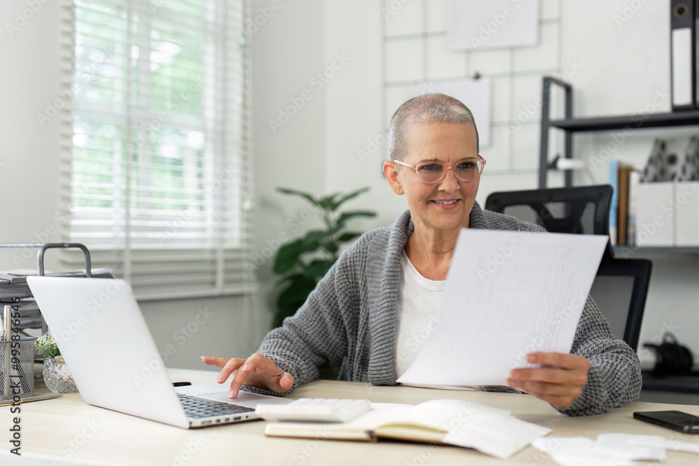 Senior Woman Working from Home on Laptop, Reviewing Documents in Modern Home Office Setting Senior Woman Working from Home on Laptop, Reviewing Documents in Modern Home Office Setting