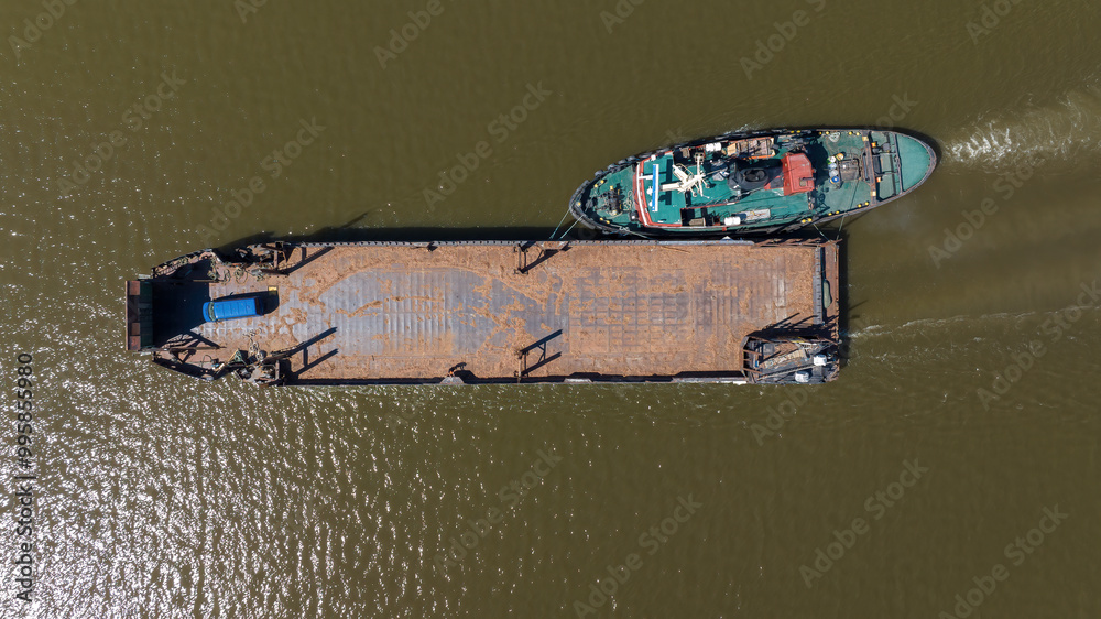 Fototapeta premium Tug boat pushing barge secured on the side. Aerial top down view.