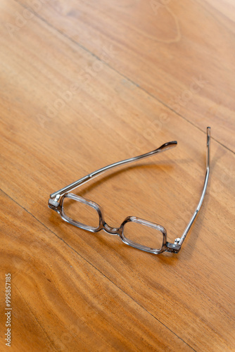 A pair of reading glasses resting on a wooden table in a cozy indoor setting during the afternoon