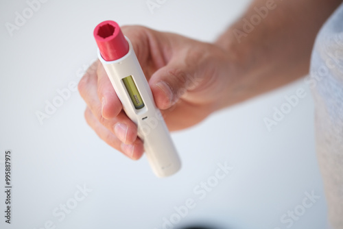 Detail of An anonymous man with pen injector in his hand for a biological or insulin type medical treatment. It is a modern injectable healthcare drug such as Adalimumab, Etanercept or epinephrine