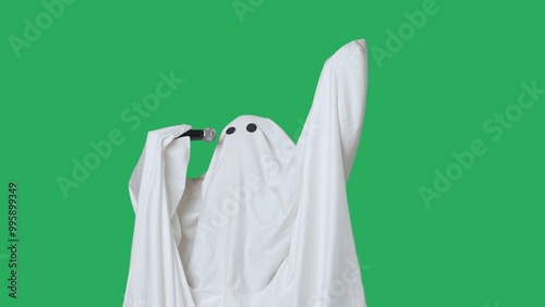 Fototapeta kuchenna Funny halloween ghost in white sheet singing son in karaoke microphone, isolated on chroma key green screen background. Happy halloween spooky concept.