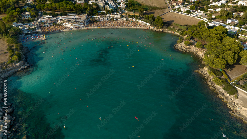 Aerial view of the beach of Lido Gandoli in the municipality of Leporano, near Taranto, in Puglia, Italy. There are many people under the umbrellas and in the sea. Aerial view of the beach of Lido Gandoli in the municipality of Leporano, near Taranto, in Puglia, Italy. There are many people under the umbrellas and in the sea.
