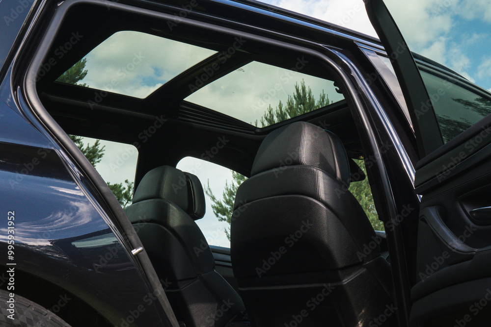 The view through the open back door of the car shows the glass roof and the dark leather interior. Low angle view up against a blue cloudy sky. The view through the open back door of the car shows the glass roof and the dark leather interior. Low angle view up against a blue cloudy sky.
