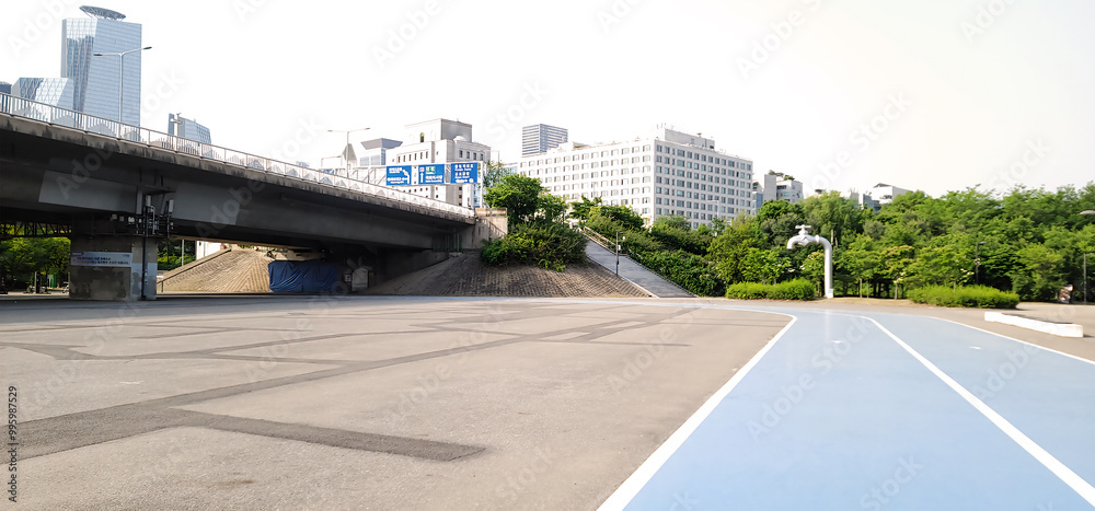 blue running track, on a city park, in Seoul, a paved area with a blue-painted section, surrounded by lush green trees and bushes. buildings and structures, on a sunny day with a clear sky blue running track, on a city park, in Seoul, a paved area with a blue-painted section, surrounded by lush green trees and bushes. buildings and structures, on a sunny day with a clear sky
