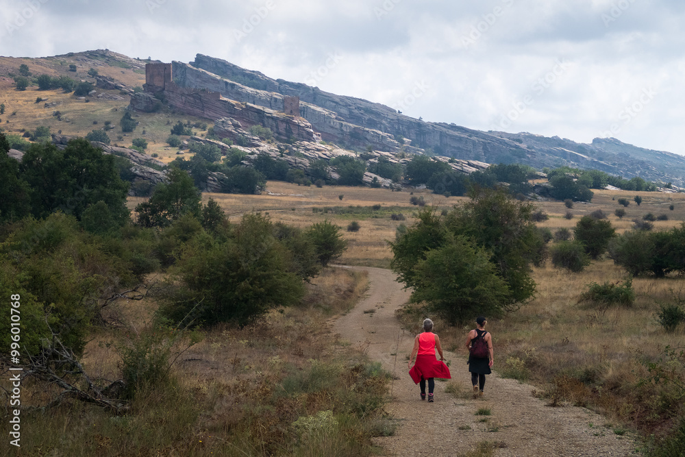 Obraz premium Dos mujeres senderistas caminan por la sierra de Caldereros hacia el castillo de Zafra, Campillo de Dueñas, Guadalajara, España.