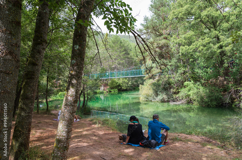 Una pareja de senderistas descansan frente a una pasarela que cruza el río Tajo, parque natural del Alto Tajo, Guadalajara, España. Una pareja de senderistas descansan frente a una pasarela que cruza el río Tajo, parque natural del Alto Tajo, Guadalajara, España.