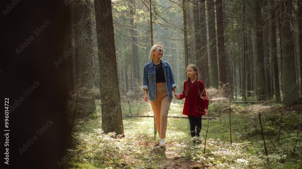 Mother and daughter walking together along pathway in woodland. Blonde woman embraces girl strolling in forest, enjoying active leisure on holiday. Family bonding Mother and daughter walking together along pathway in woodland. Blonde woman embraces girl strolling in forest, enjoying active leisure on holiday. Family bonding