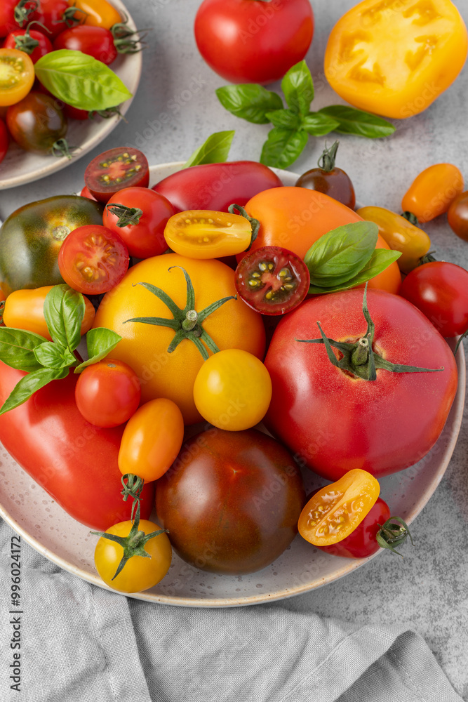 Mixed colorful ripe tomatoes on retro ceramic plate with linen napkin on grey stone table background. Red, green, pink, orange and yellow fresh tomato varieties closeup. Mixed colorful ripe tomatoes on retro ceramic plate with linen napkin on grey stone table background. Red, green, pink, orange and yellow fresh tomato varieties closeup.