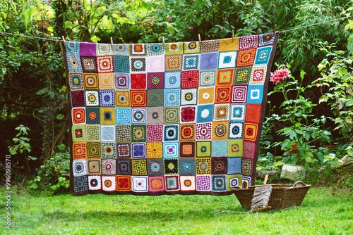 Fotografie Vintage crochet blanket made from cotton granny squares hanging outdoors on the string with rustic laundry wicker basket