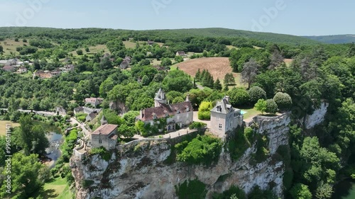 A breathtaking aerial view of a historic village nestled in lush green hills. The scene features a beautiful castle  on a cliffside, overlooking a river flowing through the valley. 