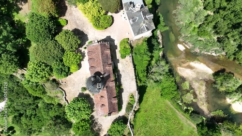 A breathtaking aerial view of a historic village nestled in lush green hills. The scene features a beautiful castle  on a cliffside, overlooking a river flowing through the valley. 