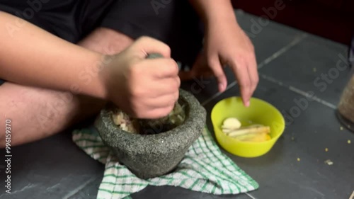 A man using a stone mortar and pestle to grinding and crushing ingredients for cooking at the kitchen floor. 