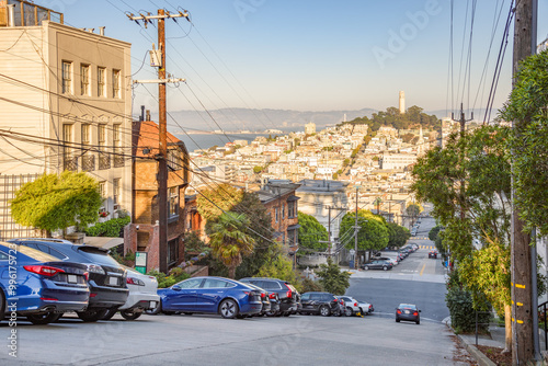 Steep street with car parked along the kerb in San Francisco on a sunny autumn day. Coit tower is visible in distance.