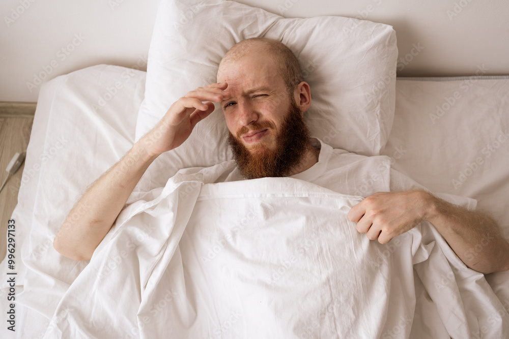 Bearded handsome man lying in bed at home suffering from headache or hangover wake-up in the morning. people, bedtime and rest concept Bearded handsome man lying in bed at home suffering from headache or hangover wake-up in the morning. people, bedtime and rest concept