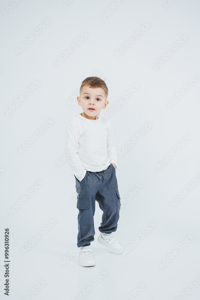 A boy in a white longsleeve and joggers on a white background. Cheerful boy in stylish clothes. A boy in a white longsleeve and joggers on a white background. Cheerful boy in stylish clothes.