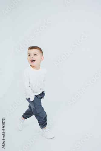 A boy in a white longsleeve and joggers on a white background. Cheerful boy in stylish clothes.