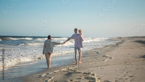 A young perents holds her little daughter by the hand and together they walk along the ocean towards the sunset. photo