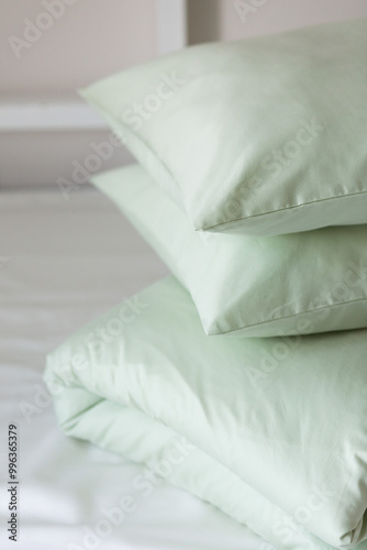 A set of light green bed linen, neatly folded in a pile: a pillow in a pillowcase and a blanket in a duvet cover on a blue sheet. Minimalist bedroom. Cozy home concept. Scandinavian style