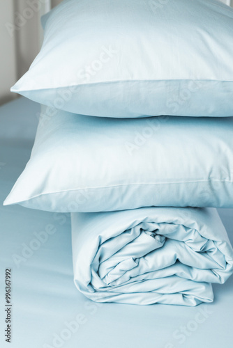 A set of blue bed linen, neatly folded in a pile: a pillow in a pillowcase and a blanket in a duvet cover on a blue sheet. Minimalist bedroom. Cozy home concept. Scandinavian style