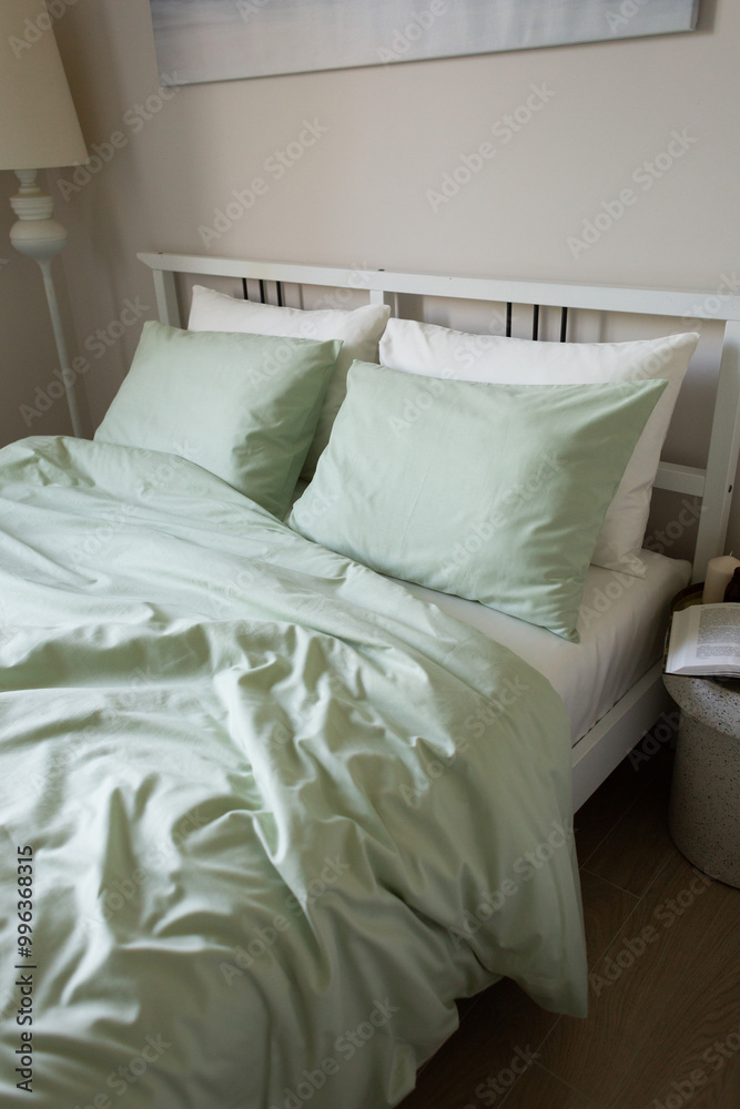 Obraz premium Light green unmade bed in the morning in elegant minimalistic bedroom. Interior design and lifestyle. Cozy home concept.