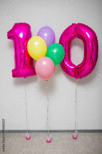 pink number 10 balloons and bunch of bright helium balloons on white background
