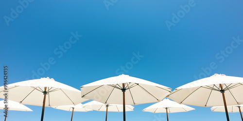 A view of white umbrellas against a vivid blue sky with scattered clouds, embodying the essence of a serene, sunny summer day.