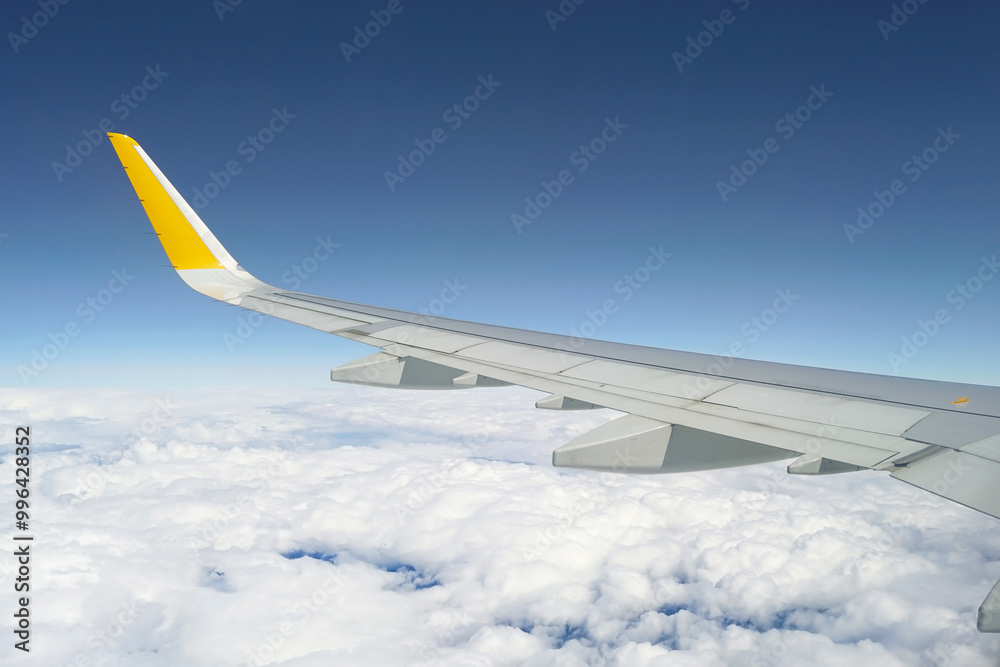 Obraz premium The wing of a large passenger plane flying above the clouds. The view seen from the plane window by tourists, migrants and people returning home from vacation.