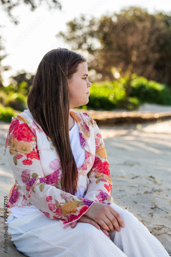 First Nations Australian Torres Strait Islander teen girl sitting on beach sand dune looking away First Nations Australian Torres Strait Islander teen girl sitting on beach sand dune looking away