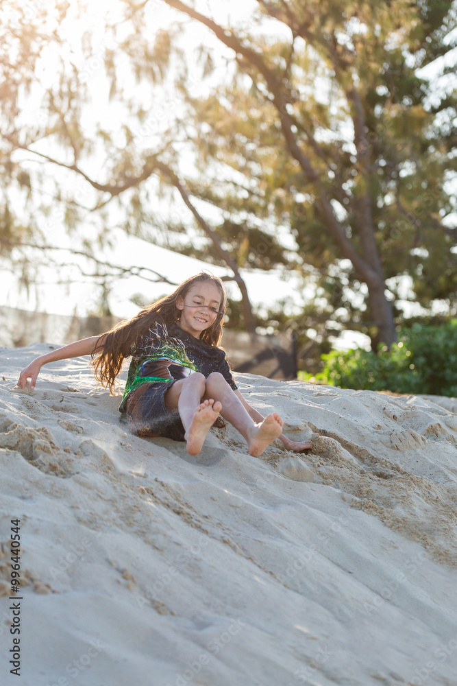 First Nations Australian Torres Strait Islander kid rolling down sand dune at the beach First Nations Australian Torres Strait Islander kid rolling down sand dune at the beach