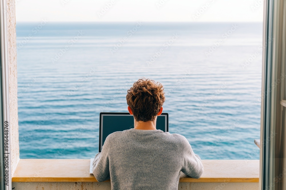 Fototapeta premium Person working on laptop with sea view from a balcony.