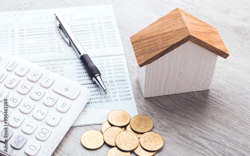 House model, coin pile, calculator, and savings account passbook are placed on the table, symbolizing the concept of house financing, savings, and financial planning for real estate investment photo