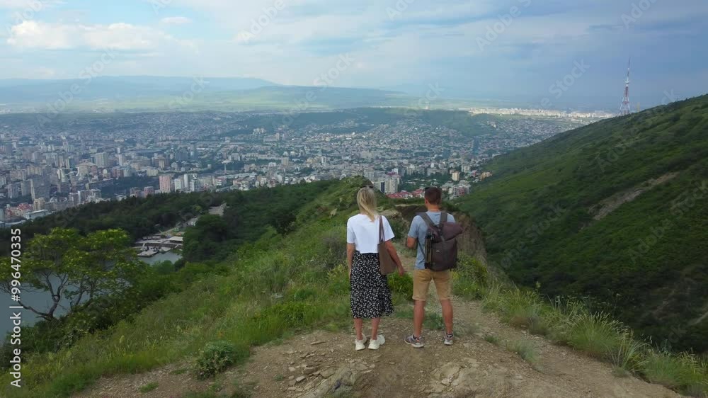 Couple of tourists enjoying breathtaking panoramic view of Tbilisi, Georgia, from hilltop observation deck, immersing themselves in stunning cityscape and vibrant atmosphere. Shooting from drone. Couple of tourists enjoying breathtaking panoramic view of Tbilisi, Georgia, from hilltop observation deck, immersing themselves in stunning cityscape and vibrant atmosphere. Shooting from drone.