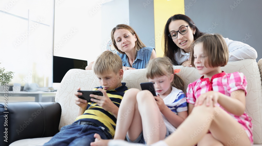 Portrait of kids play online games on mobile phones and mums control watching them. Addiction to smartphone from young age. Childhood, technology concept Portrait of kids play online games on mobile phones and mums control watching them. Addiction to smartphone from young age. Childhood, technology concept