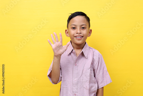 Smart asian schoolboy standing while showing five fingers. Isolated on yellow with copyspace photo