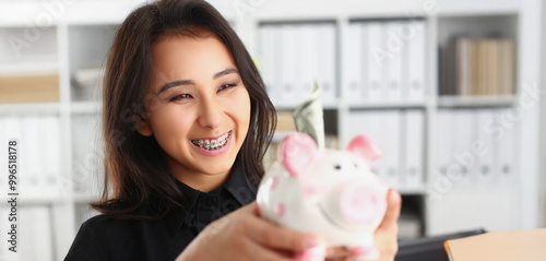 Portrait of pretty laughing young woman holding piggybank with banknote in it. Smiling brunette female save up for future. Investment, budget, fund concept photo