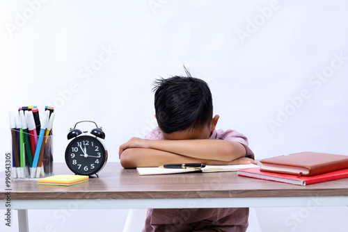 Tired asian schoolboy studying in classroom while writing on the book. Isolated on white background