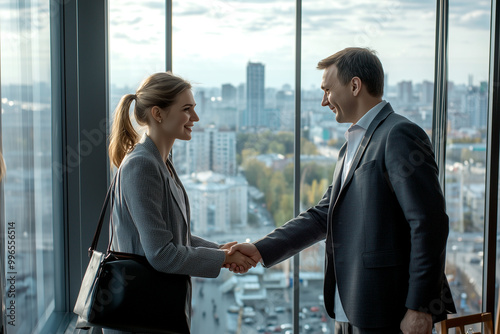 A warm handshake between a smiling woman and a man during a formal gathering in a city building, promoting unity and collaboration.