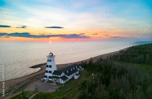 West Point lighthouse stands prominently on the coastline as the sun sets over the calm ocean waters, illuminating the sky with vibrant hues of orange and yellow, Prince Edward Island, Canada